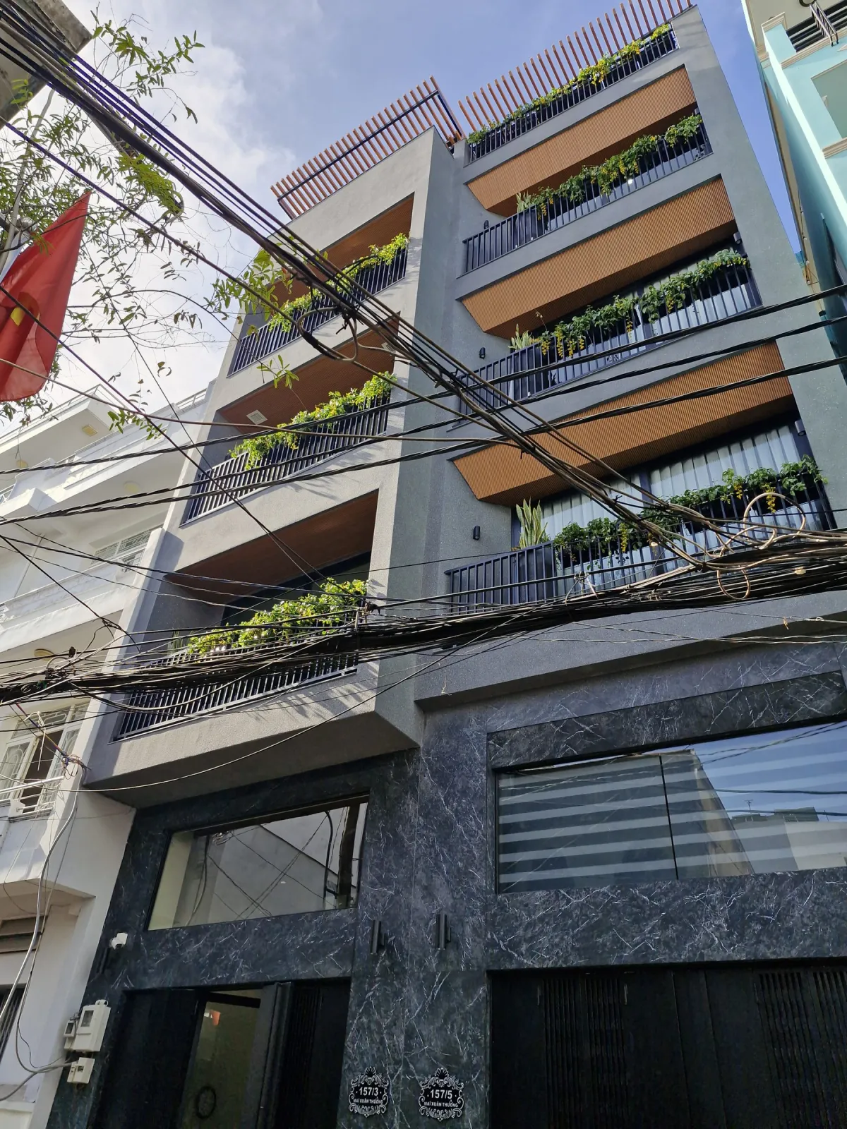 Mặt tiền MXT House với ban công cây xanh và ốp gỗ